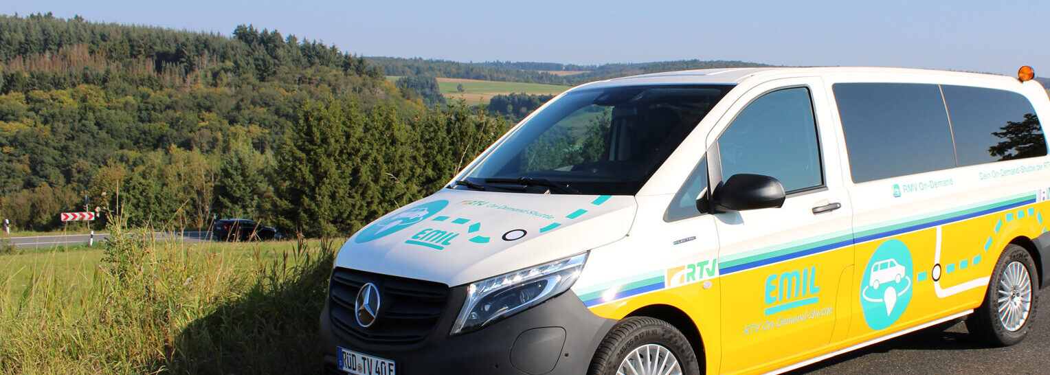 Das elektrisch betriebene On-Demand-Shuttle „EMIL“ der Rheingau-Taunus-Verkehrsgesellschaft steht vor dem historischen Idsteiner Schloss mit weiß-roter Fassade und markantem Schieferdach.